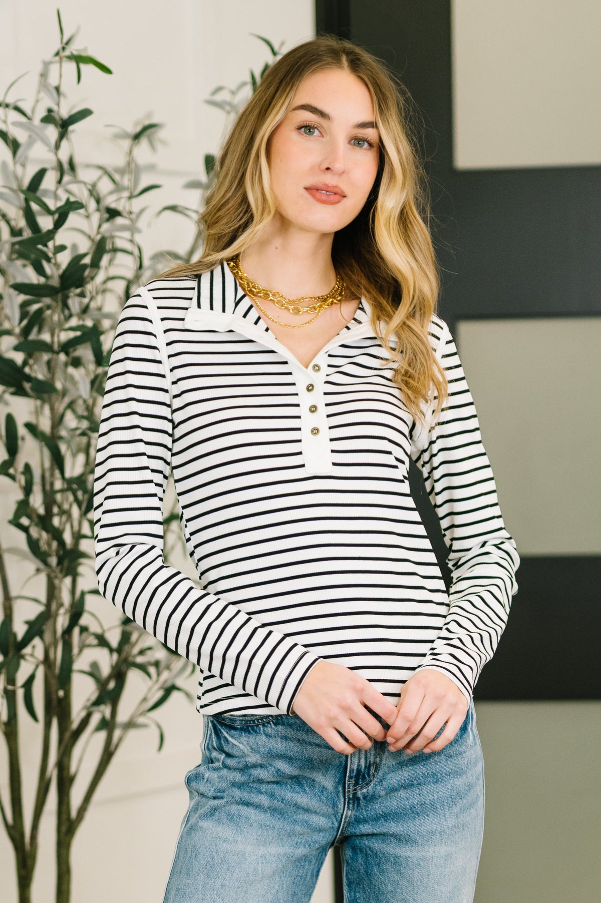 Woman wearing a black and white striped long-sleeve top with blue jeans indoors.
