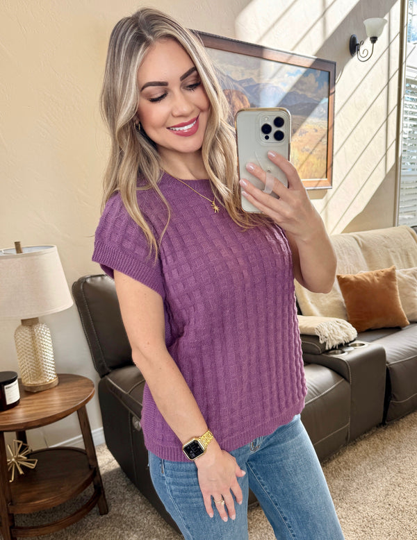 Woman taking a selfie in a purple sweater and blue jeans in a living room.