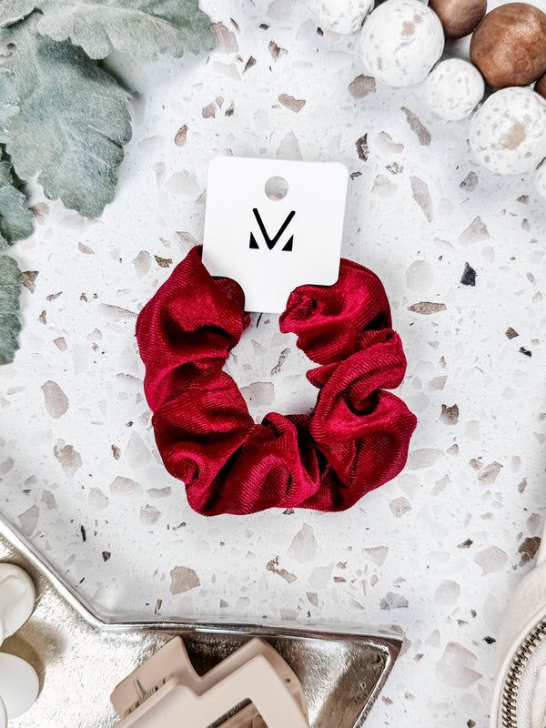 Red scrunchie on a white and gray speckled surface with a brand tag.