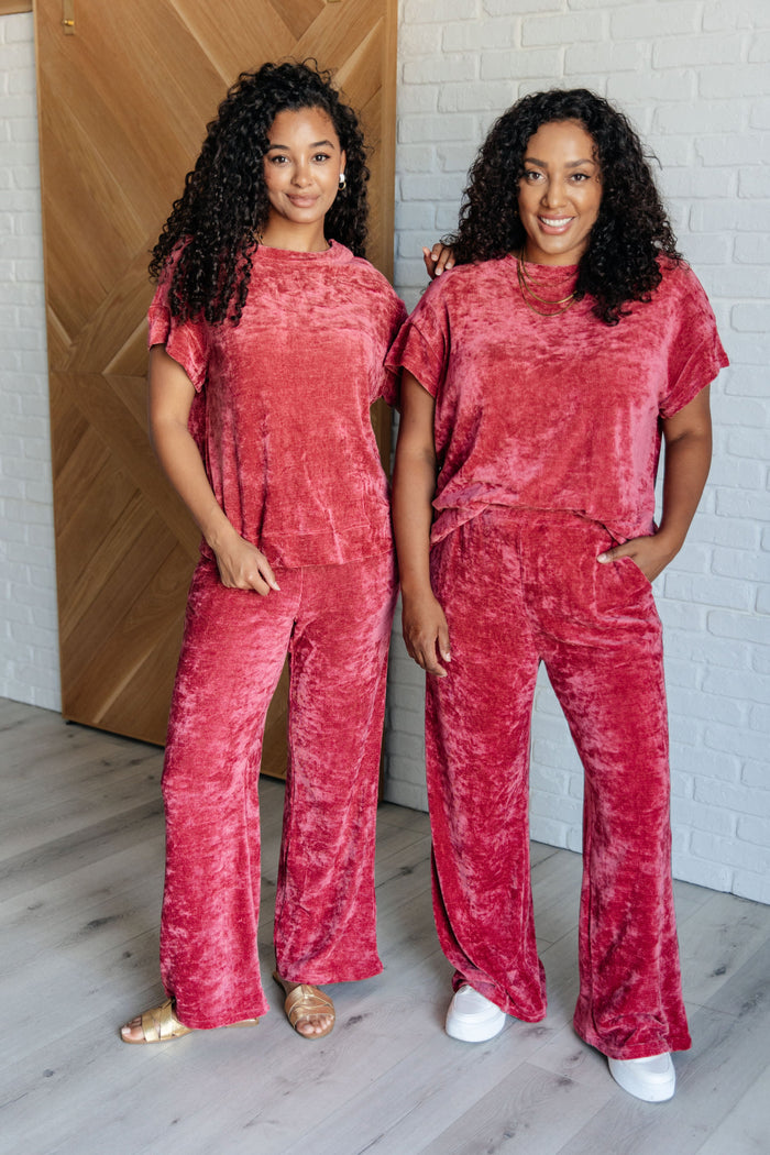 Two women standing in a room, wearing matching red velour sets with boatneck tops and elastic waist pants, posing for the camera.