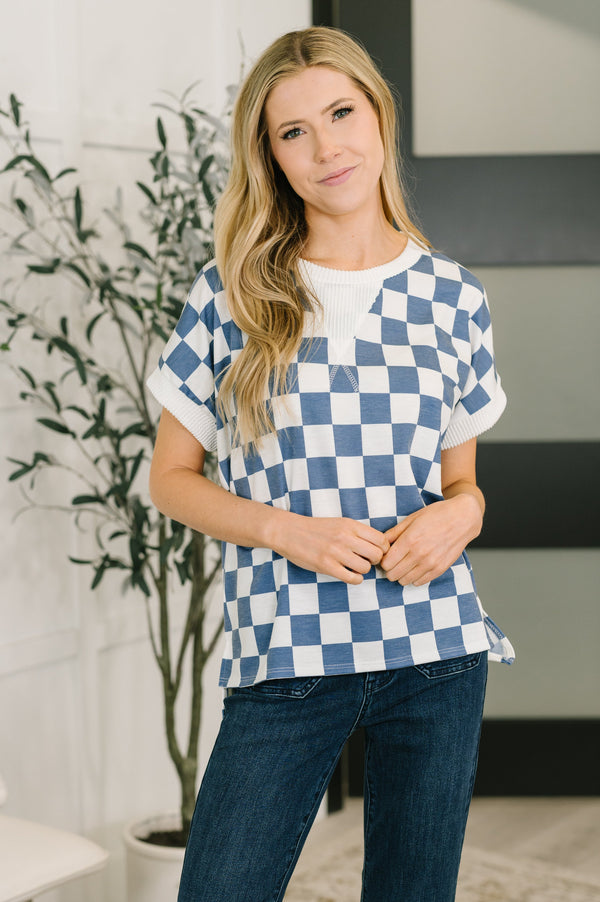 Woman wearing a blue and white checkered shirt and jeans indoors.