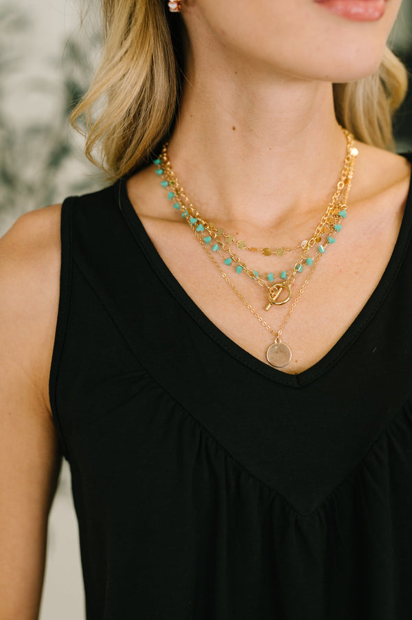 Woman wearing a black top with layered gold and turquoise necklaces.