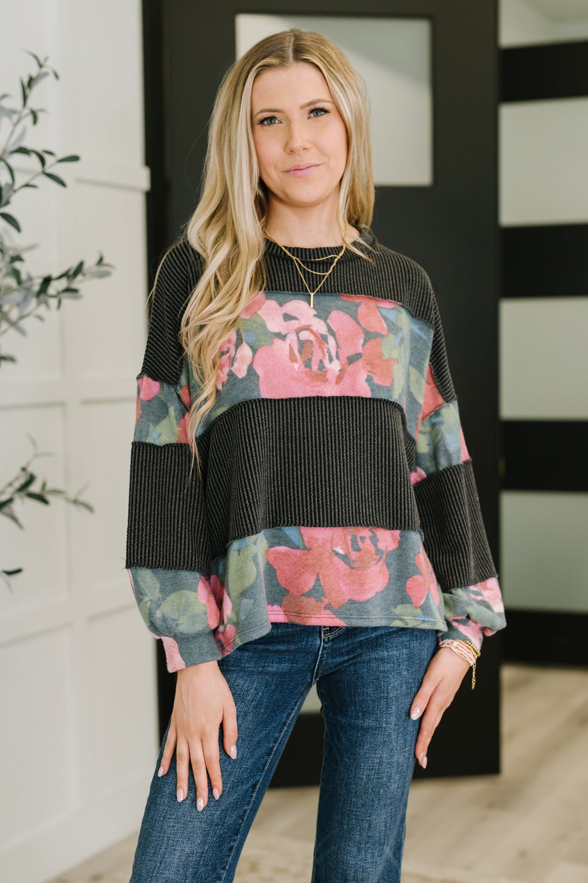 Woman wearing a floral sweater with black accents and blue jeans indoors.