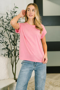 Woman wearing a pink t-shirt and blue jeans indoors with a plant and striped wall in the background