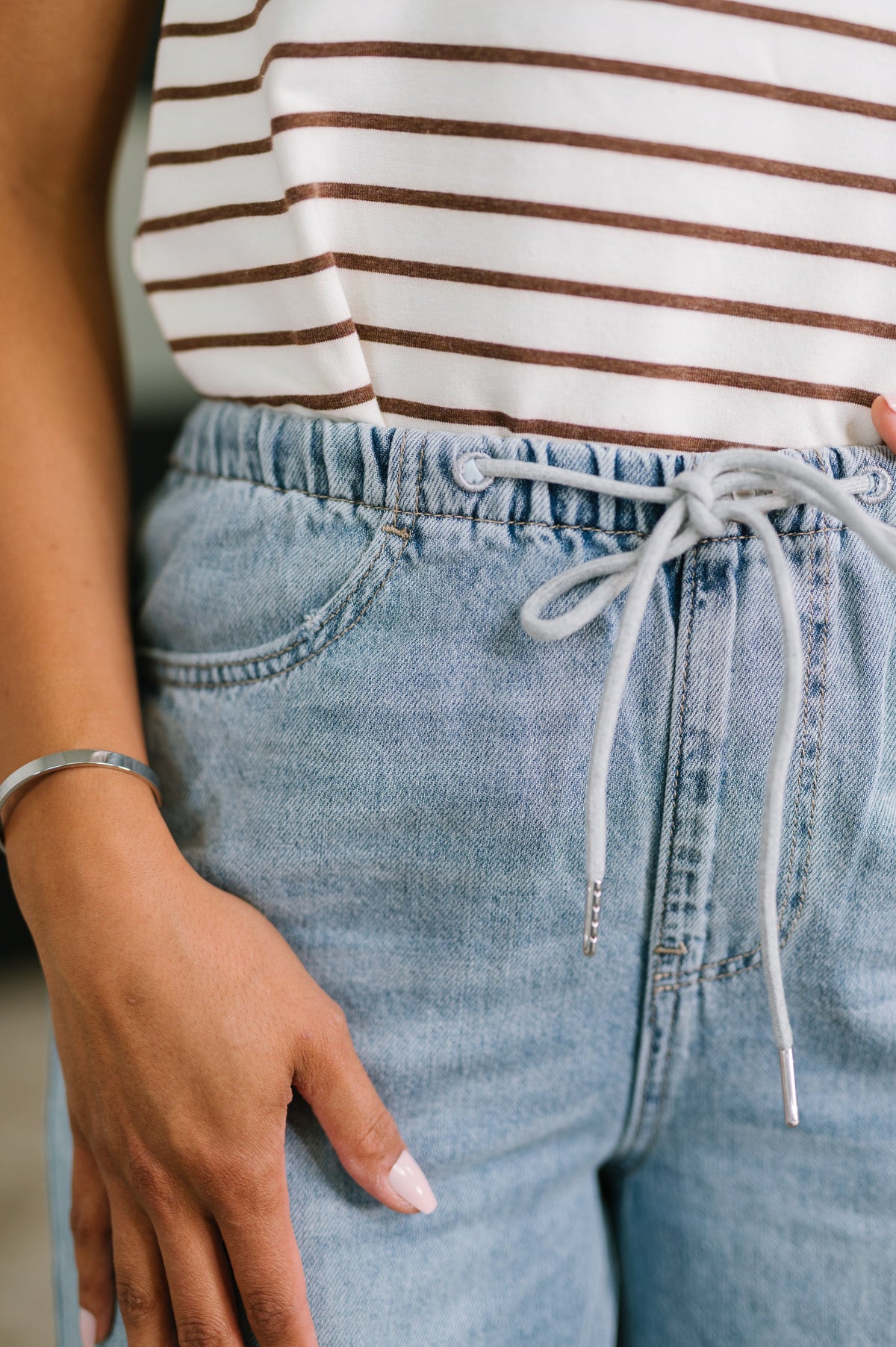 Close-up of a person wearing a striped shirt and blue jeans with a blurred background
