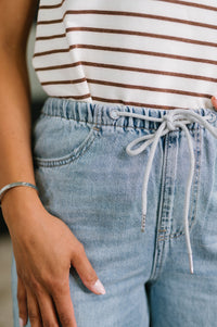 Close-up of a person wearing a striped shirt and blue jeans with a blurred background