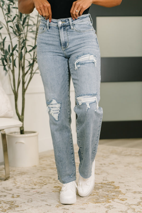 Person wearing light blue ripped jeans and white sneakers in an indoor setting.