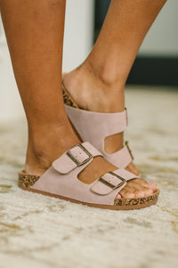 Pink sandals with gold buckles worn by a person on a light background