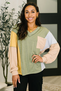Woman wearing a green, yellow, and beige color-blocked sweater indoors.