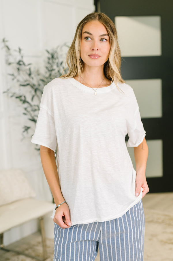 Woman wearing a white top and striped pants in a room with a plant and bench.