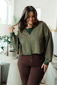 Woman wearing a green sweater and brown pants in a bright room.
