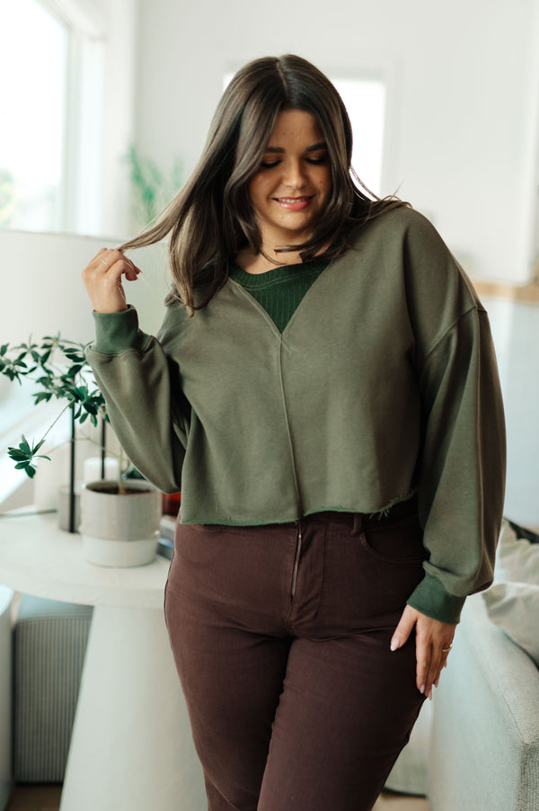Woman wearing a green sweater and brown pants in a bright room.
