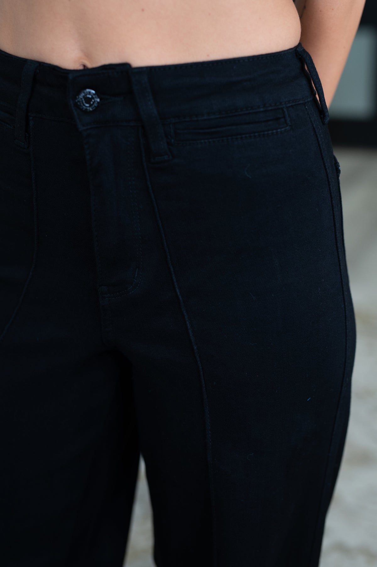 Close-up of a person wearing dark navy or near-black denim pants, showing the waistband, button, belt loops, front pocket, and thigh area.