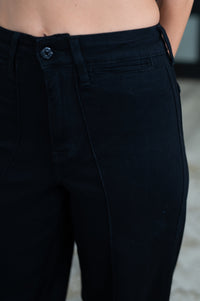 Close-up of a person wearing dark navy or near-black denim pants, showing the waistband, button, belt loops, front pocket, and thigh area.
