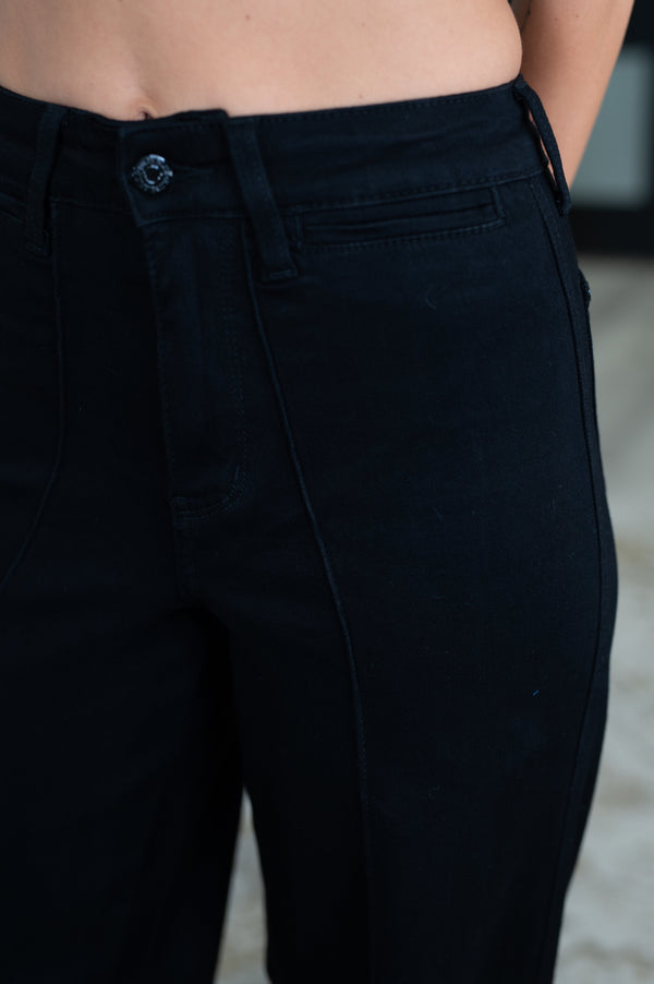 Close-up of a person wearing dark navy or near-black denim pants, showing the waistband, button, belt loops, front pocket, and thigh area.