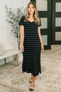Woman wearing a black and white striped dress in a room with a plant and bench.