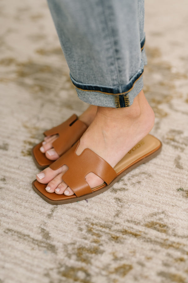 Brown sandals worn with rolled-up jeans on a textured surface