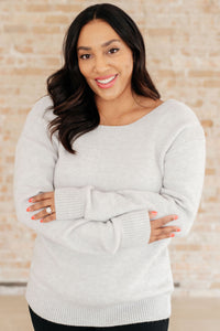 Woman wearing a light gray sweater with a wooden wall background