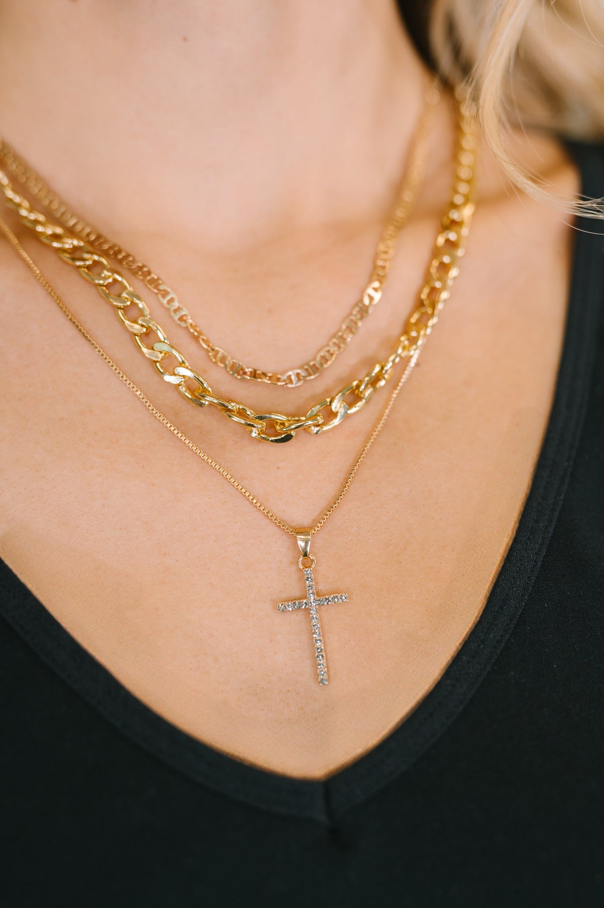 Close-up of a person wearing multiple gold necklaces with a cross pendant.