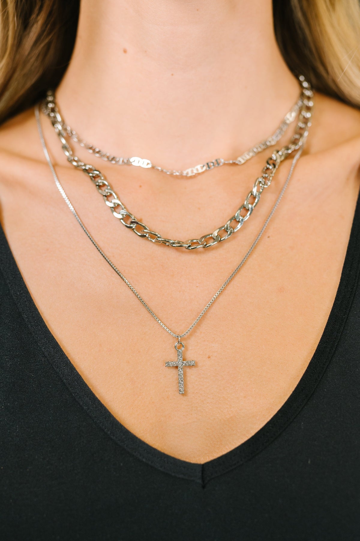 Close-up of layered necklaces with a cross pendant on a black top