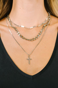 Close-up of layered necklaces with a cross pendant on a black top