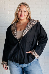 Woman wearing a black jacket with leopard print trim against a white brick wall.