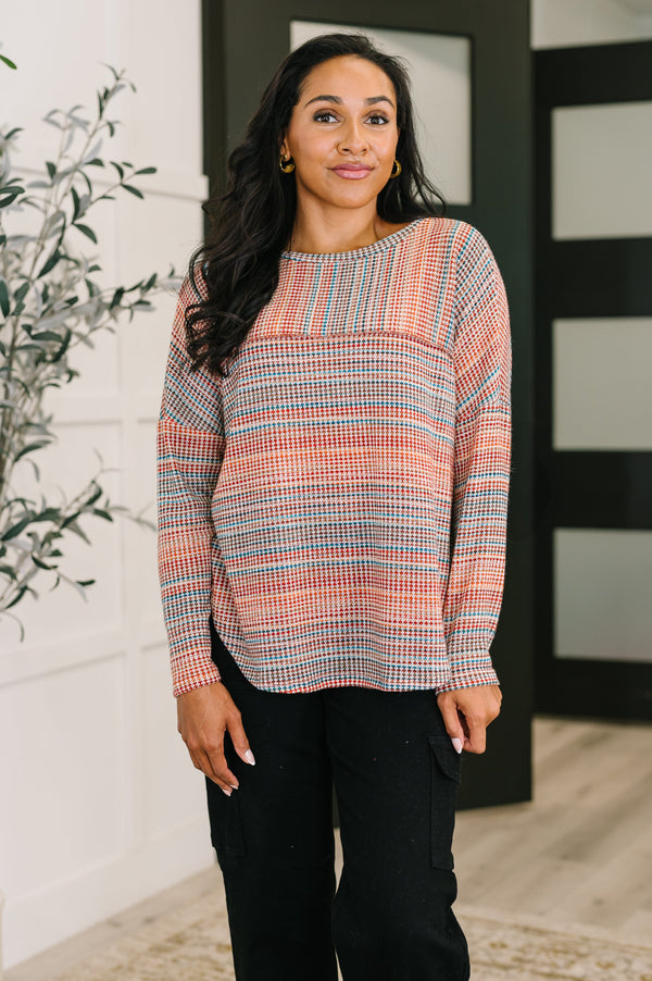 Woman wearing a plaid sweater standing indoors with a plant and door in the background