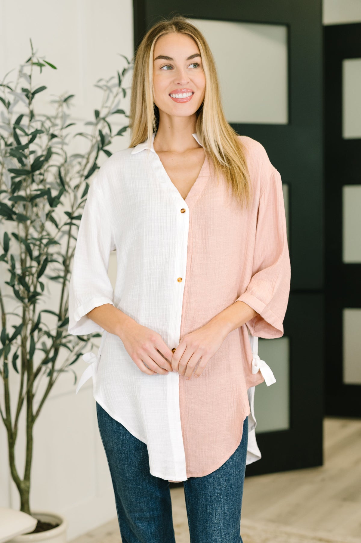 Woman wearing a light pink kimono-style garment over a white shirt with blue jeans, standing indoors.