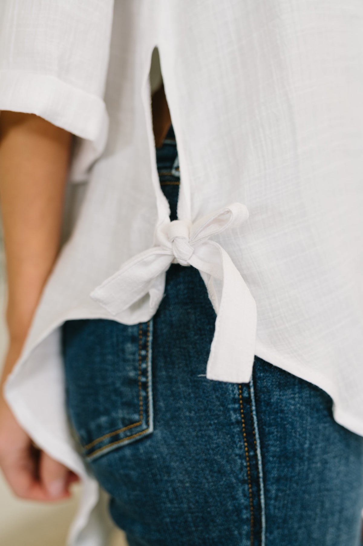 White blouse with a bow detail worn over blue jeans on a blurred background