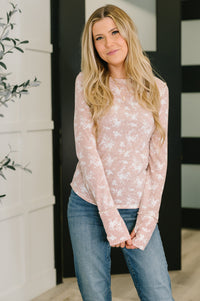 Woman wearing a light pink floral long-sleeve top and blue jeans indoors.