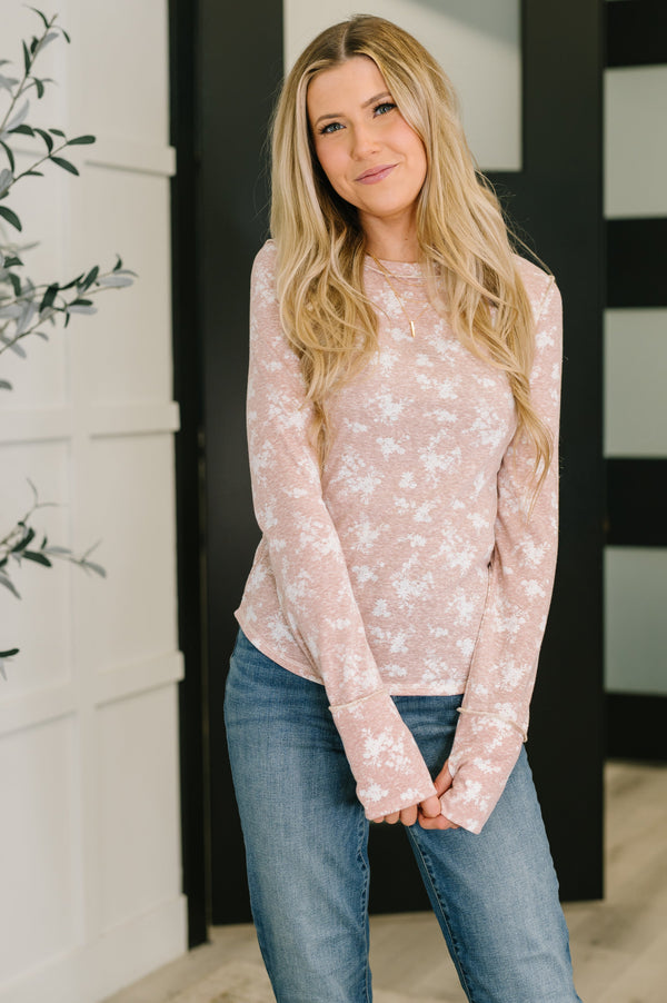 Woman wearing a light pink floral long-sleeve top and blue jeans indoors.