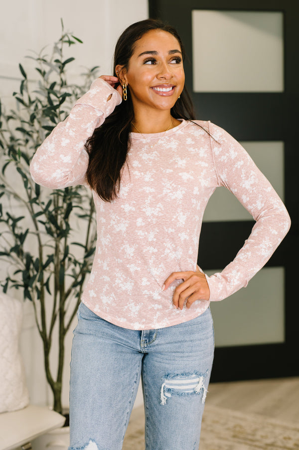 Woman wearing a pink floral long-sleeve top and blue jeans indoors.