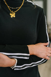 Person wearing a black outfit with white stripes and gold jewelry, including a necklace and bracelet.