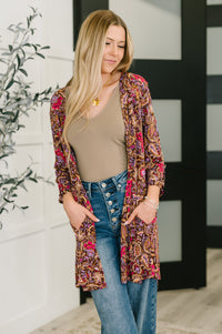 Woman wearing a floral cardigan over a beige top and blue jeans, standing indoors.
