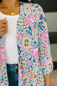 Person wearing a colorful floral cardigan over a white shirt and jeans.