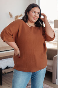 Woman wearing a brown sweater and blue jeans indoors.