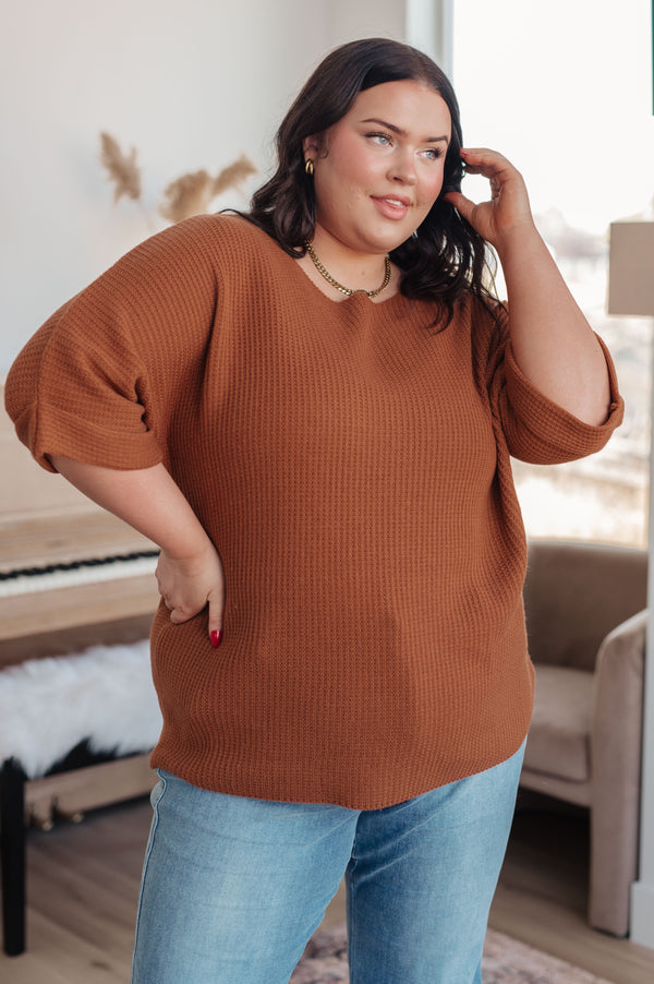 Woman wearing a brown sweater and blue jeans indoors.