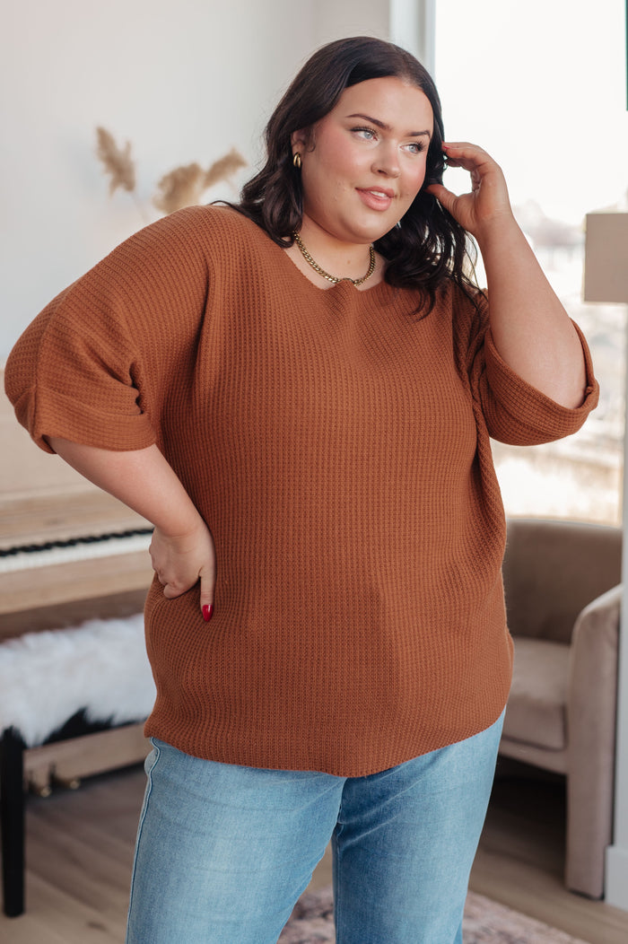 Woman wearing a brown sweater and blue jeans indoors.