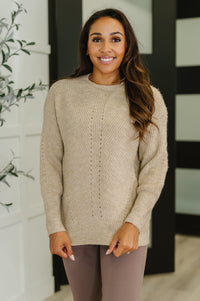 Woman wearing a beige sweater and pants standing indoors with a decorative background