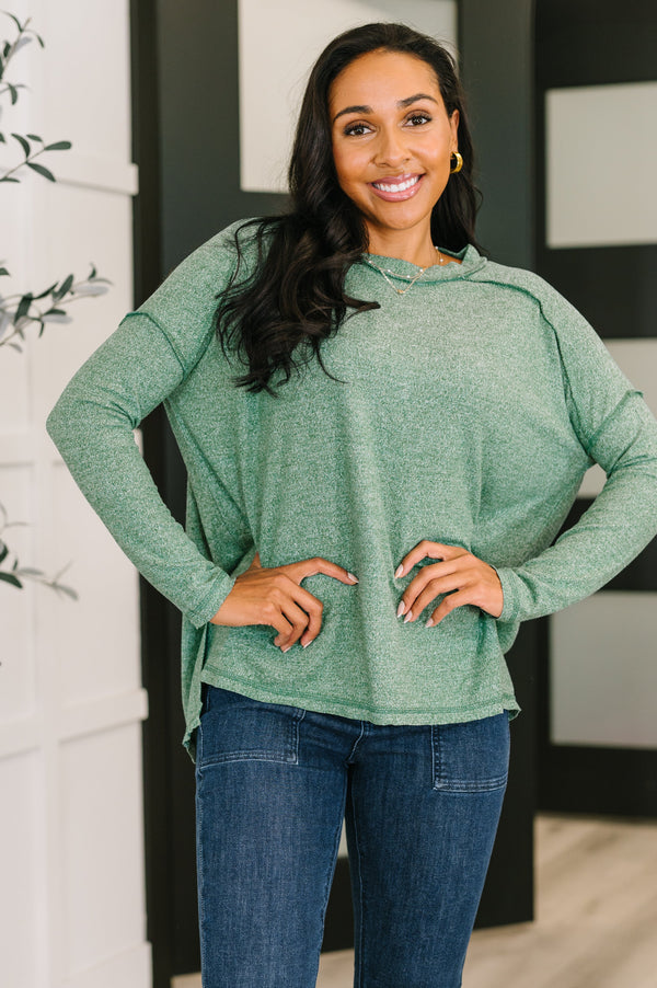 Woman wearing a green long-sleeve top and blue jeans indoors.