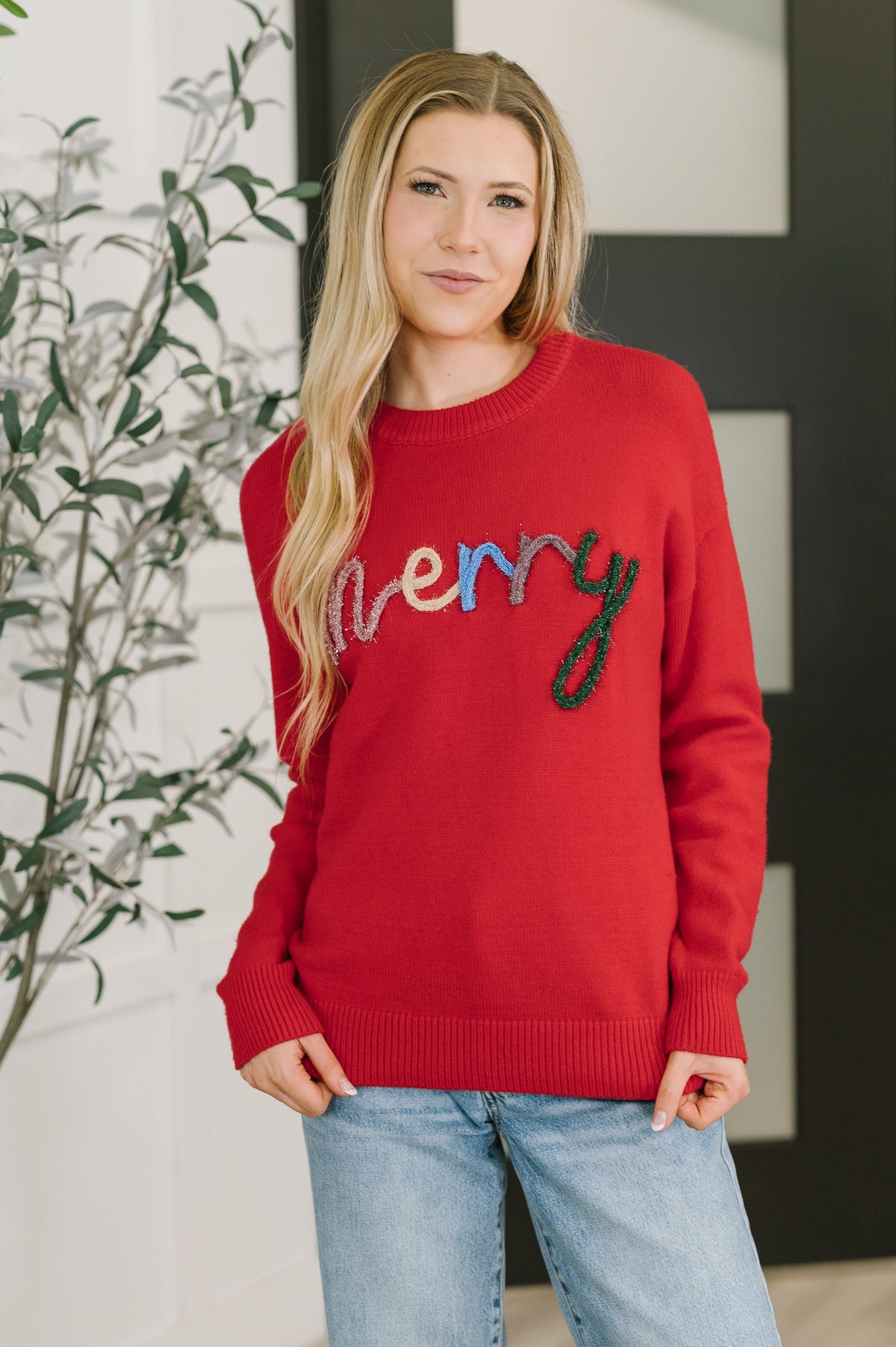 Person wearing a red sweater with colorful text, standing indoors.