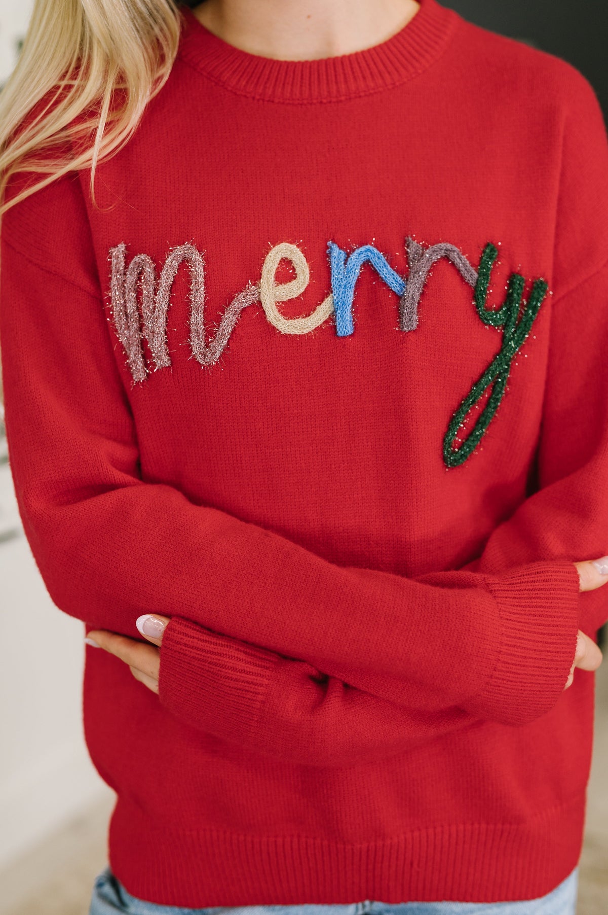 Red sweater with colorful 'merry' text worn by a person.