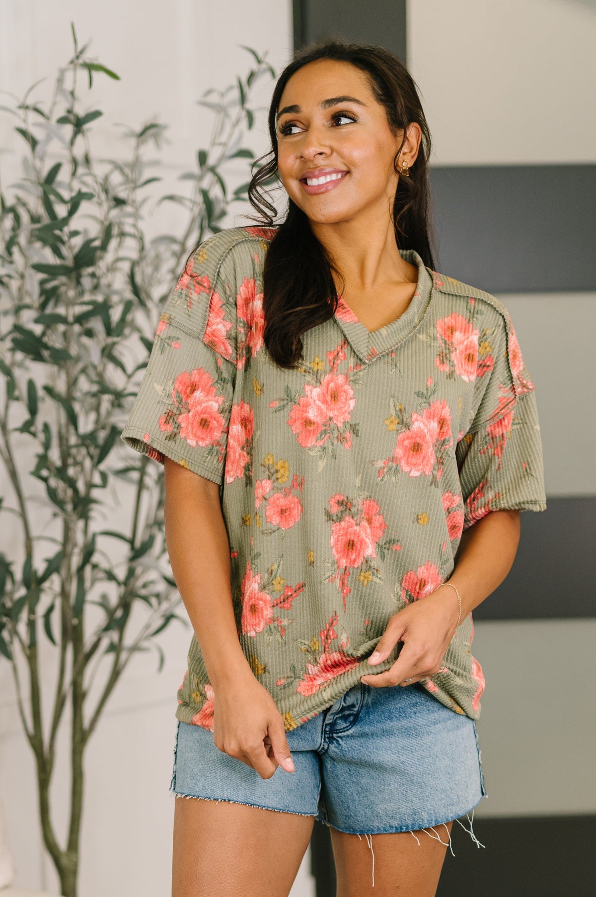 Woman wearing a floral oversized shirt and denim shorts indoors.