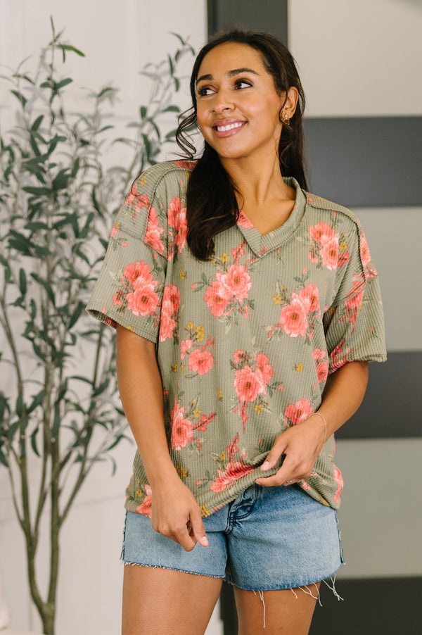 Woman wearing a floral oversized shirt and denim shorts indoors.