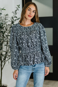 Woman wearing a black and white patterned blouse and blue jeans indoors.