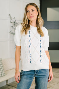 Woman wearing a white sweater with blue accents in a living room setting