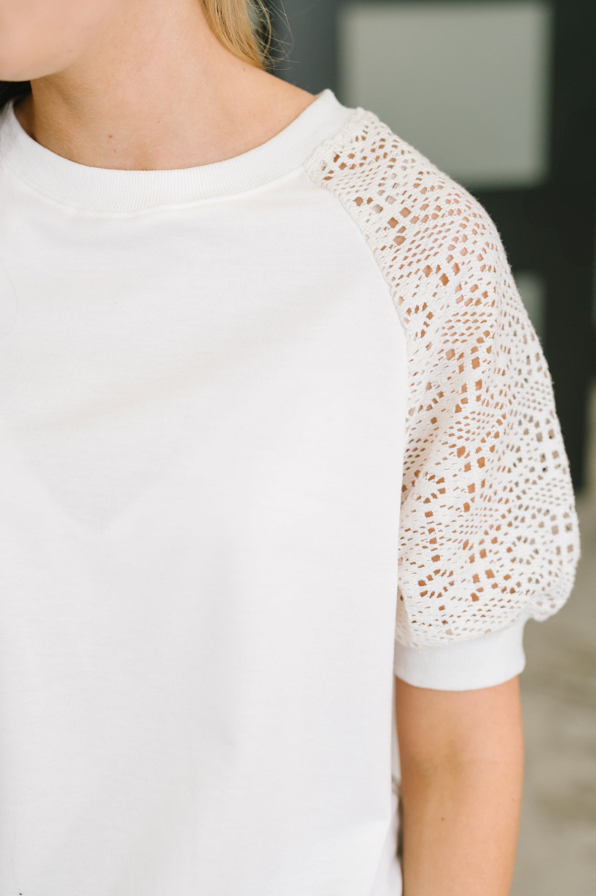Close-up of a person wearing a white short-sleeve top with textured openwork crochet lace sleeves.