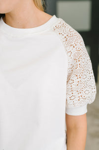 Close-up of a person wearing a white short-sleeve top with textured openwork crochet lace sleeves.