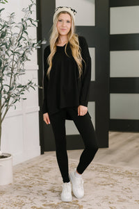 Woman wearing a black outfit with white sneakers in a room with a plant and striped wall.