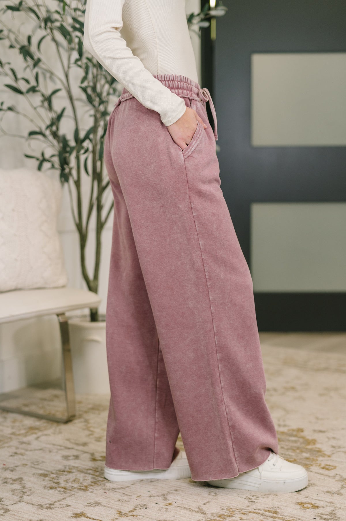 Person wearing pink wide-leg pants in a room with a plant and furniture.